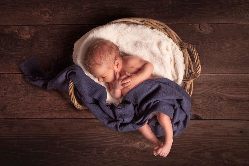 photographe-lille-hauts-de-france-bebe-david-plichon Photographe naissance à Lille nouveau-né dans corbeille en osier et tissu bleu marine sur fond bois